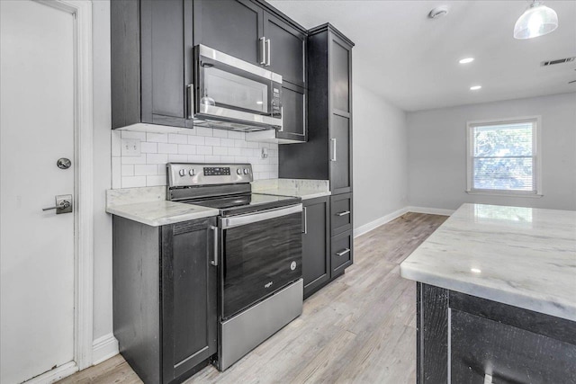 kitchen featuring light wood-style flooring, dark cabinetry, stainless steel appliances, decorative backsplash, and light stone countertops