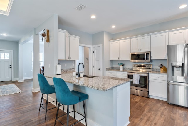 kitchen with appliances with stainless steel finishes, kitchen peninsula, dark hardwood / wood-style floors, white cabinets, and sink