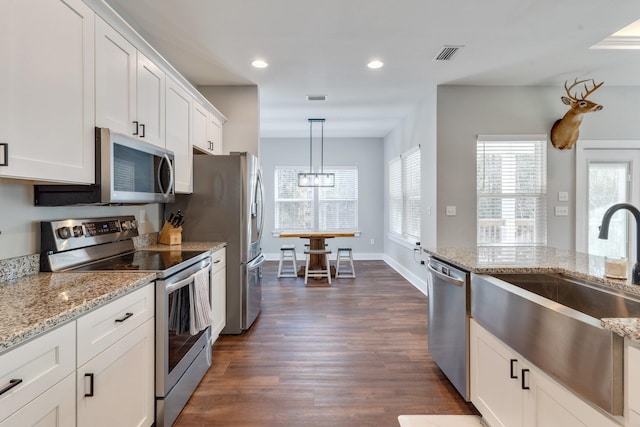 kitchen with white cabinets, light stone counters, dark hardwood / wood-style floors, pendant lighting, and appliances with stainless steel finishes