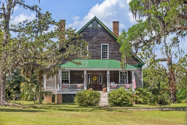view of front of home with a chimney, covered porch, and a front yard
