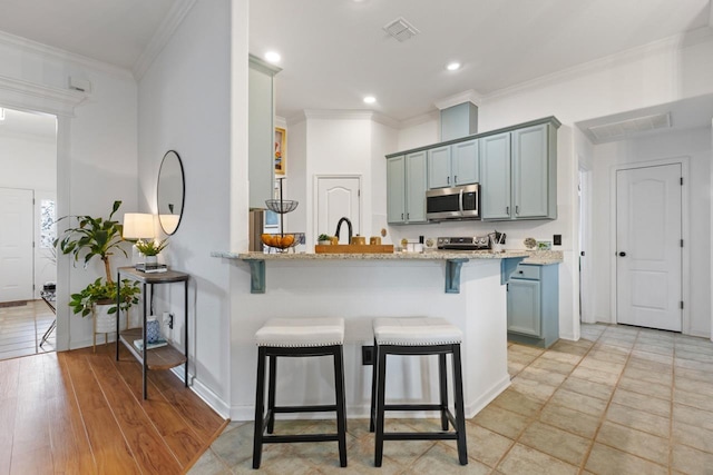 kitchen with light stone countertops, appliances with stainless steel finishes, a breakfast bar, a peninsula, and visible vents