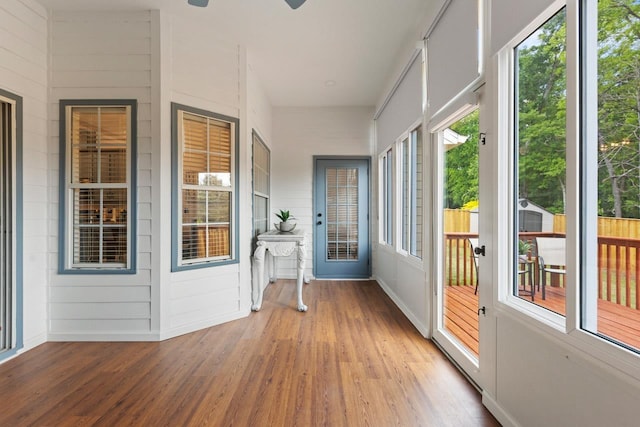 unfurnished sunroom featuring a ceiling fan, baseboards, and wood finished floors
