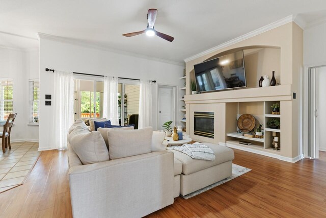 living room with a ceiling fan, baseboards, wood finished floors, a tile fireplace, and ornamental molding