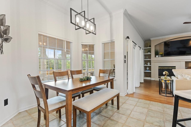 dining room with built in features, a fireplace, baseboards, a chandelier, and ornamental molding