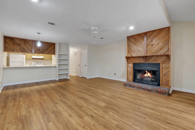 unfurnished living room with light wood-type flooring, ceiling fan, and a fireplace