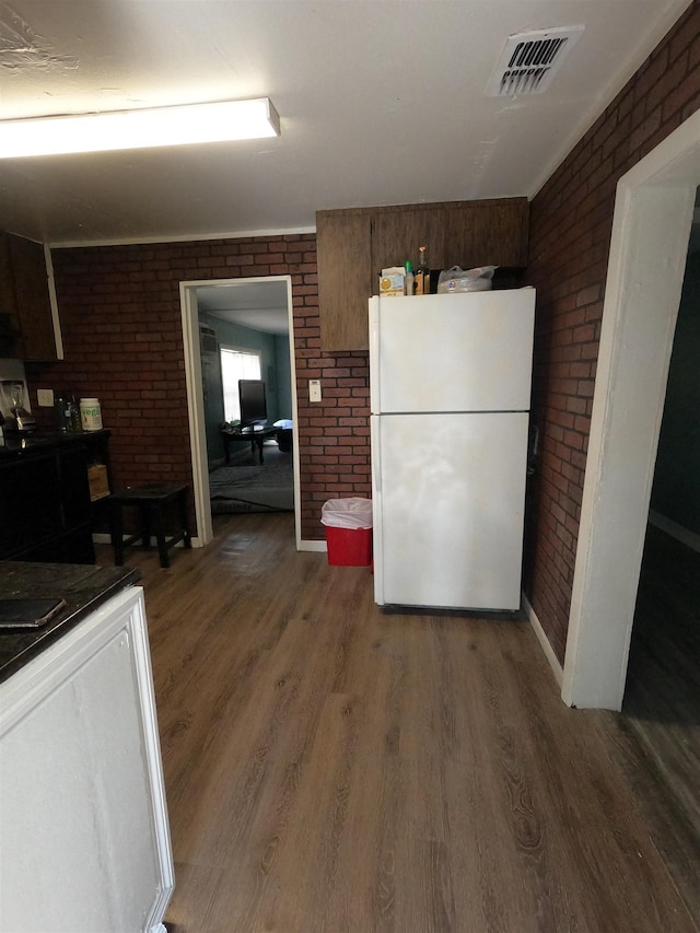 kitchen featuring dark wood-type flooring, brick wall, and white fridge