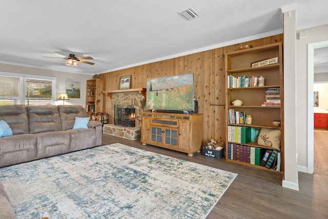 living area featuring visible vents, ceiling fan, ornamental molding, wood finished floors, and a stone fireplace