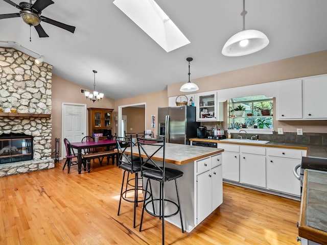 kitchen with vaulted ceiling with skylight, stainless steel fridge, and white cabinets