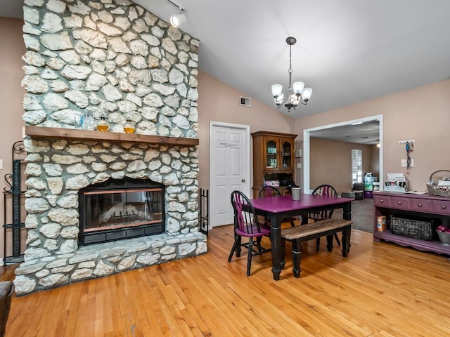 dining space featuring rail lighting, a stone fireplace, wood-type flooring, lofted ceiling, and a notable chandelier