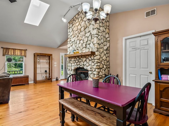 dining room featuring a stone fireplace, an inviting chandelier, track lighting, vaulted ceiling with skylight, and light wood-type flooring