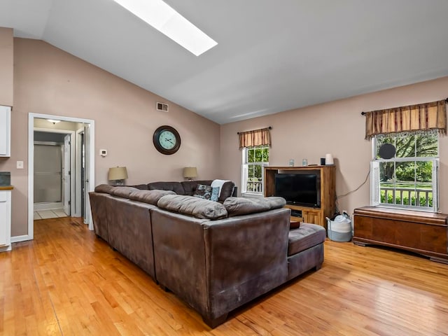 living room with vaulted ceiling with skylight and light wood-type flooring