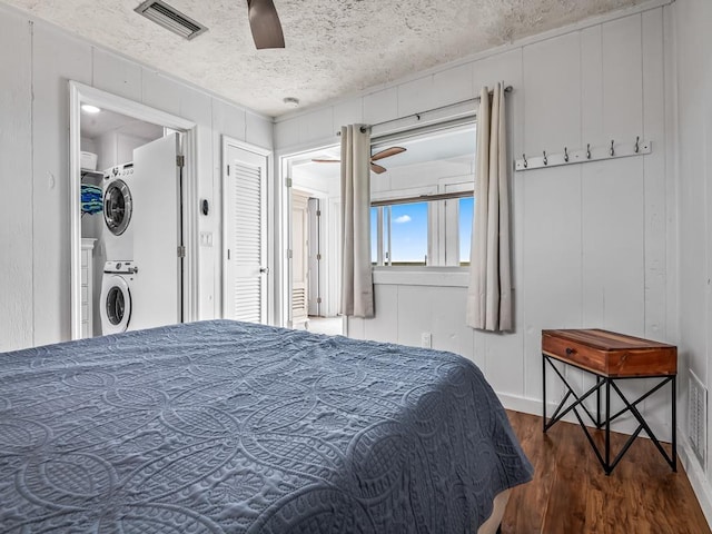 bedroom with dark wood-type flooring, stacked washer and dryer, ceiling fan, and a textured ceiling