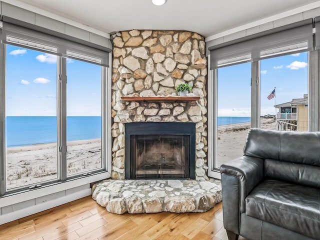 sitting room featuring a view of the beach, hardwood / wood-style floors, a stone fireplace, and a water view