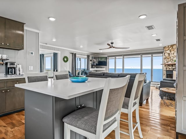 kitchen featuring a stone fireplace, a breakfast bar, a center island, dark brown cabinetry, and light hardwood / wood-style flooring