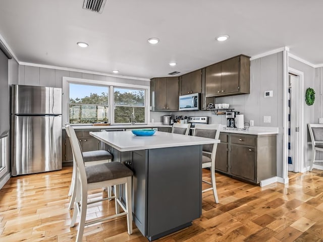 kitchen with a breakfast bar, a center island, dark brown cabinets, light hardwood / wood-style flooring, and appliances with stainless steel finishes