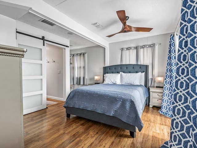 bedroom with a barn door, dark hardwood / wood-style floors, and ceiling fan