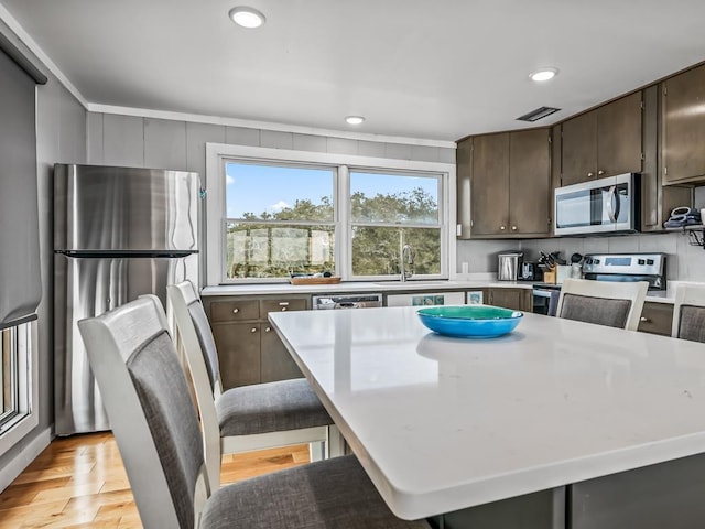 kitchen with sink, dark brown cabinets, light wood-type flooring, a kitchen island, and stainless steel appliances