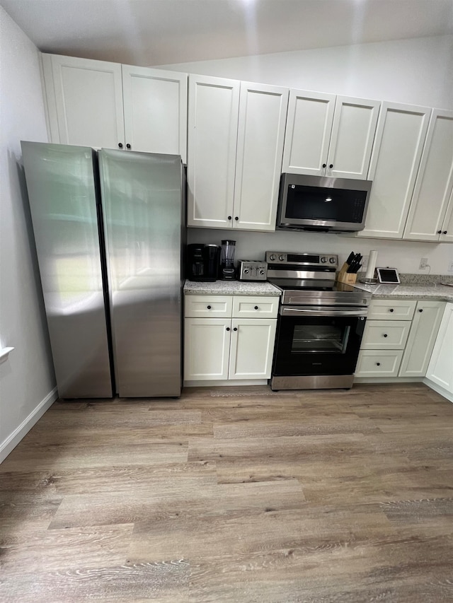 kitchen with light hardwood / wood-style floors, white cabinetry, appliances with stainless steel finishes, light stone countertops, and vaulted ceiling