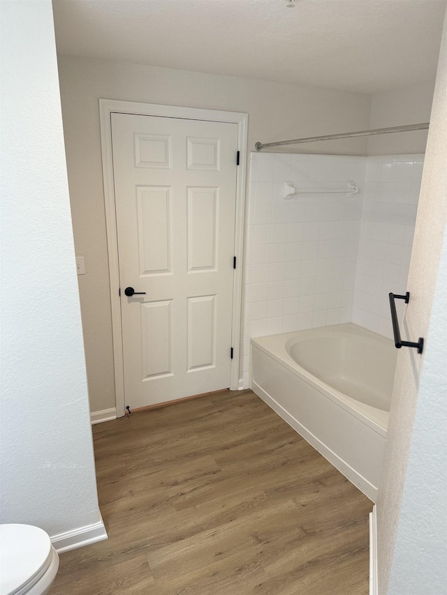 bathroom with shower / washtub combination, hardwood / wood-style floors, and toilet