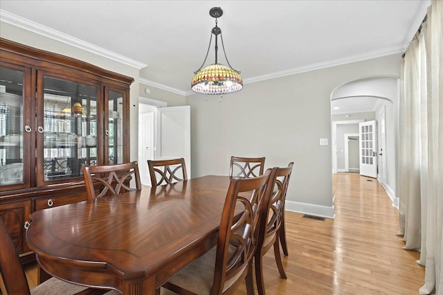 dining area with crown molding, light wood-style floors, arched walkways, baseboards, and visible vents