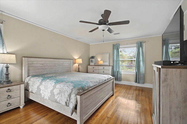bedroom with a ceiling fan, crown molding, wood finished floors, baseboards, and visible vents