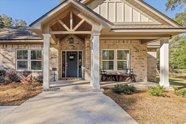 doorway to property with a porch, board and batten siding, and brick siding