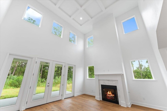 unfurnished living room with coffered ceiling, a high ceiling, a premium fireplace, beamed ceiling, and light hardwood / wood-style floors