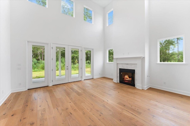 unfurnished living room featuring a wealth of natural light, a fireplace, a towering ceiling, and light wood-type flooring