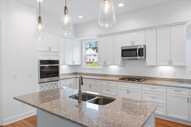 kitchen featuring appliances with stainless steel finishes, sink, a center island with sink, decorative light fixtures, and white cabinetry