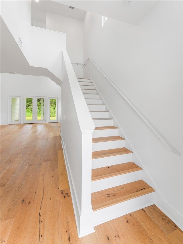 stairs featuring wood-type flooring, a towering ceiling, and french doors