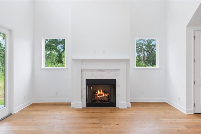 unfurnished living room featuring light hardwood / wood-style flooring, a high ceiling, and a tiled fireplace