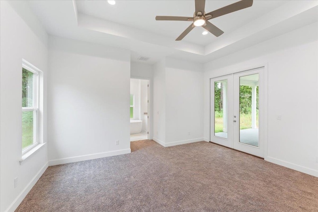 carpeted empty room with ceiling fan, a wealth of natural light, and a tray ceiling