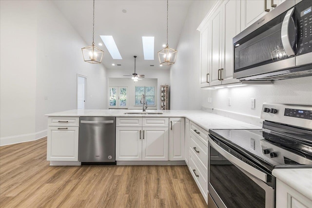 kitchen featuring sink, appliances with stainless steel finishes, white cabinetry, decorative light fixtures, and kitchen peninsula