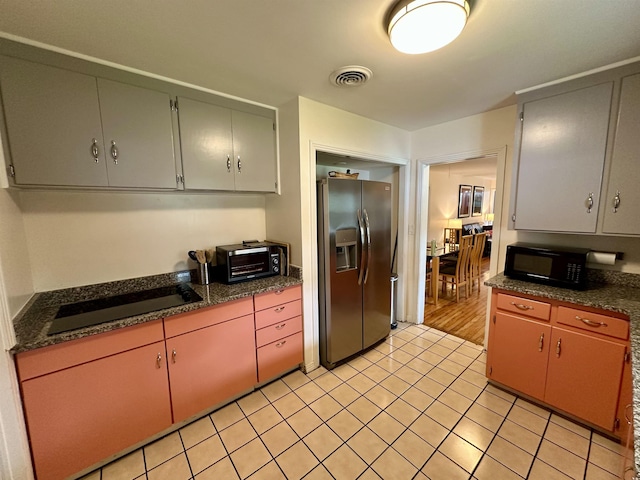 kitchen featuring light tile patterned floors, a toaster, visible vents, black appliances, and dark stone countertops