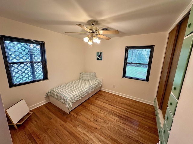 unfurnished bedroom featuring a closet, visible vents, a ceiling fan, wood finished floors, and baseboards