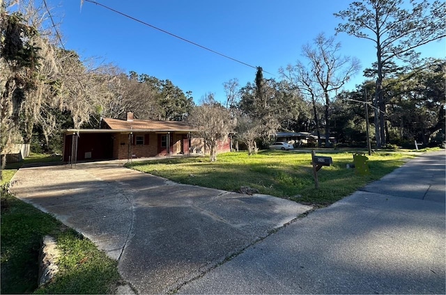 view of front facade featuring driveway, brick siding, a chimney, and a front yard