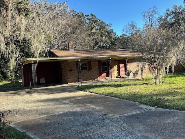 single story home with brick siding, a chimney, a front yard, a carport, and driveway