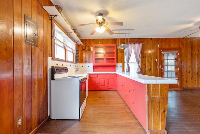 kitchen with white range with electric cooktop, wood walls, light wood-type flooring, ceiling fan, and decorative light fixtures