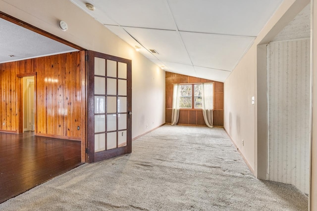 carpeted empty room featuring lofted ceiling and wooden walls