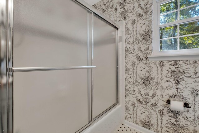 bathroom featuring shower / bath combination with glass door, baseboards, and wallpapered walls