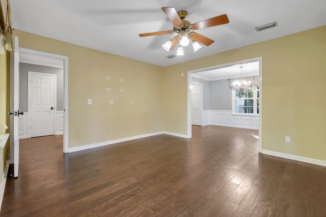 empty room featuring visible vents, a decorative wall, ceiling fan with notable chandelier, dark wood-type flooring, and a wainscoted wall