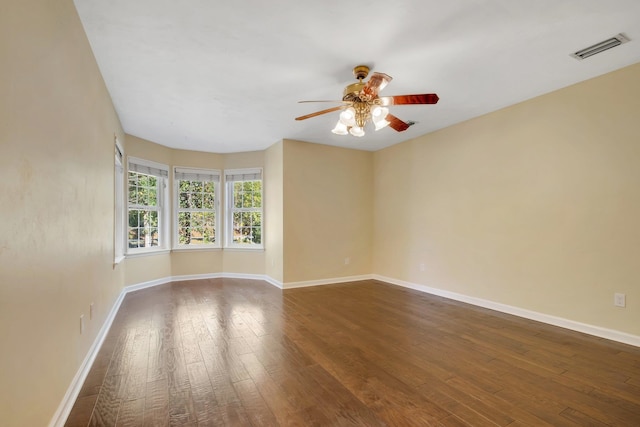 spare room featuring dark wood-type flooring, visible vents, baseboards, and a ceiling fan