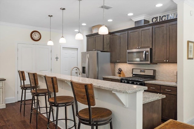 4516 Cavendish Ct, Tallahassee, FL 32309 - kitchen featuring appliances with stainless steel finishes, dark brown cabinetry, ornamental molding, a kitchen island with sink, and decorative backsplash