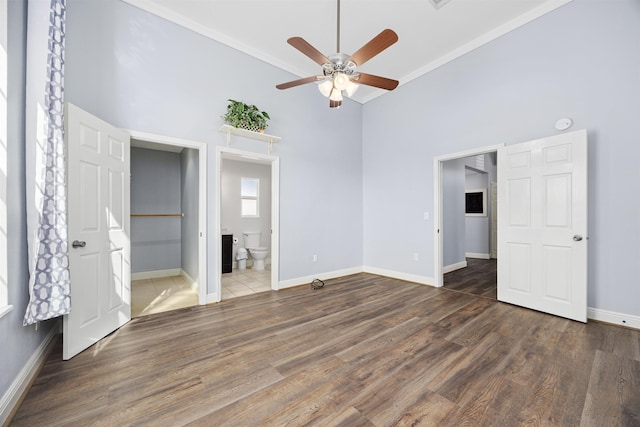 unfurnished bedroom featuring dark wood-type flooring, a high ceiling, ensuite bathroom, crown molding, and ceiling fan