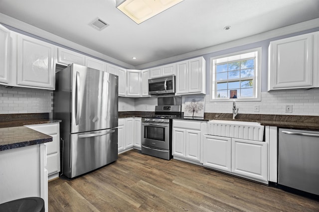 kitchen featuring appliances with stainless steel finishes, dark wood-type flooring, white cabinets, backsplash, and sink