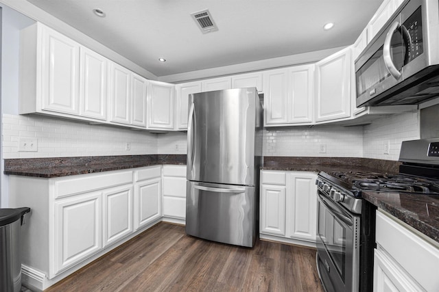 kitchen featuring appliances with stainless steel finishes, dark hardwood / wood-style flooring, white cabinetry, and dark stone countertops