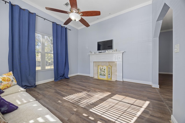 unfurnished living room featuring a tiled fireplace, dark wood-type flooring, crown molding, and ceiling fan