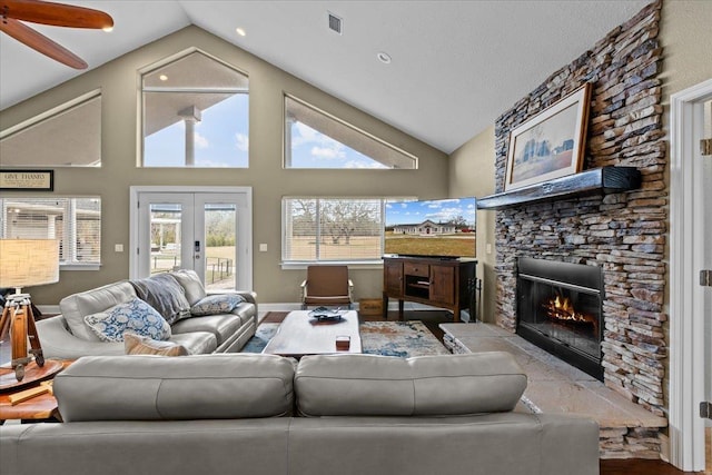 living room featuring french doors, ceiling fan, high vaulted ceiling, light hardwood / wood-style flooring, and a stone fireplace