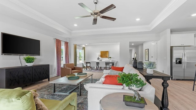 living room featuring ceiling fan, ornamental molding, a raised ceiling, and light hardwood / wood-style flooring