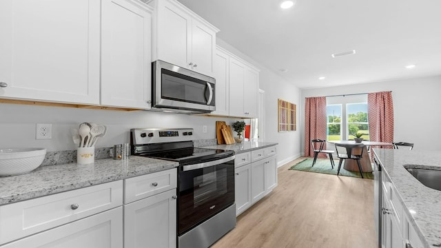 kitchen with white cabinetry, stainless steel appliances, light stone countertops, and light hardwood / wood-style flooring